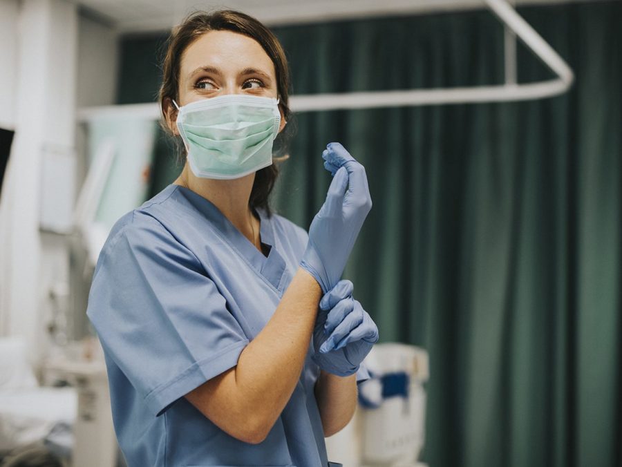 Female Nurse With A Mask Putting On Gloves